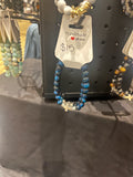 Blue tiger eye beaded bracelet with silver-tone accents and a cross detail hanging on a jewelry display.