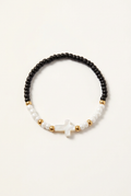 Black and white seed bead bracelet with a white cross and gold-colored spacers on a soft-white background