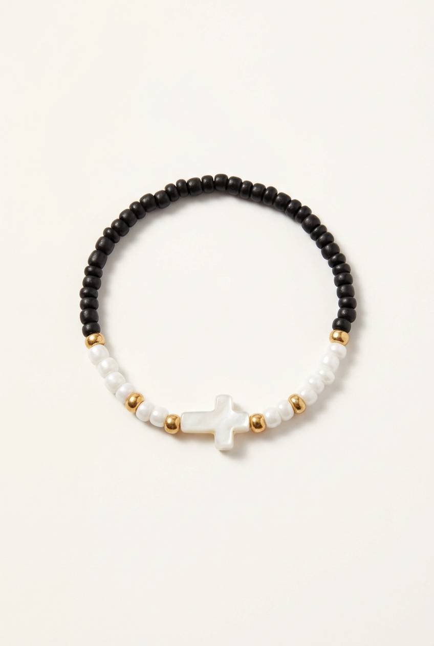 Black and white seed bead bracelet with a white cross and gold-colored spacers on a soft-white background