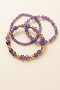 Three purple amethyst bracelets with gold-plated spacers on a warm ivory background