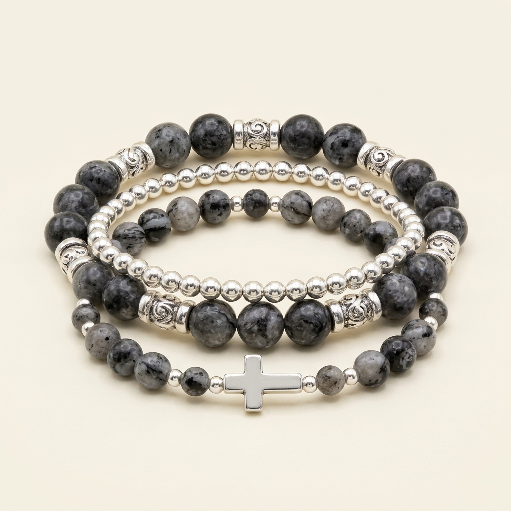 Black larvikite and silver-colored three-bracelet stack with a silver cross on an ivory background