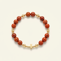 Red jasper bracelet with gold-plated spacers and a gold-colored cross arranged in a circle on a warm ivory background