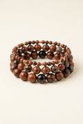 Handmade mahogany obsidian three-bracelet stack with gold-plated accents on a warm ivory background