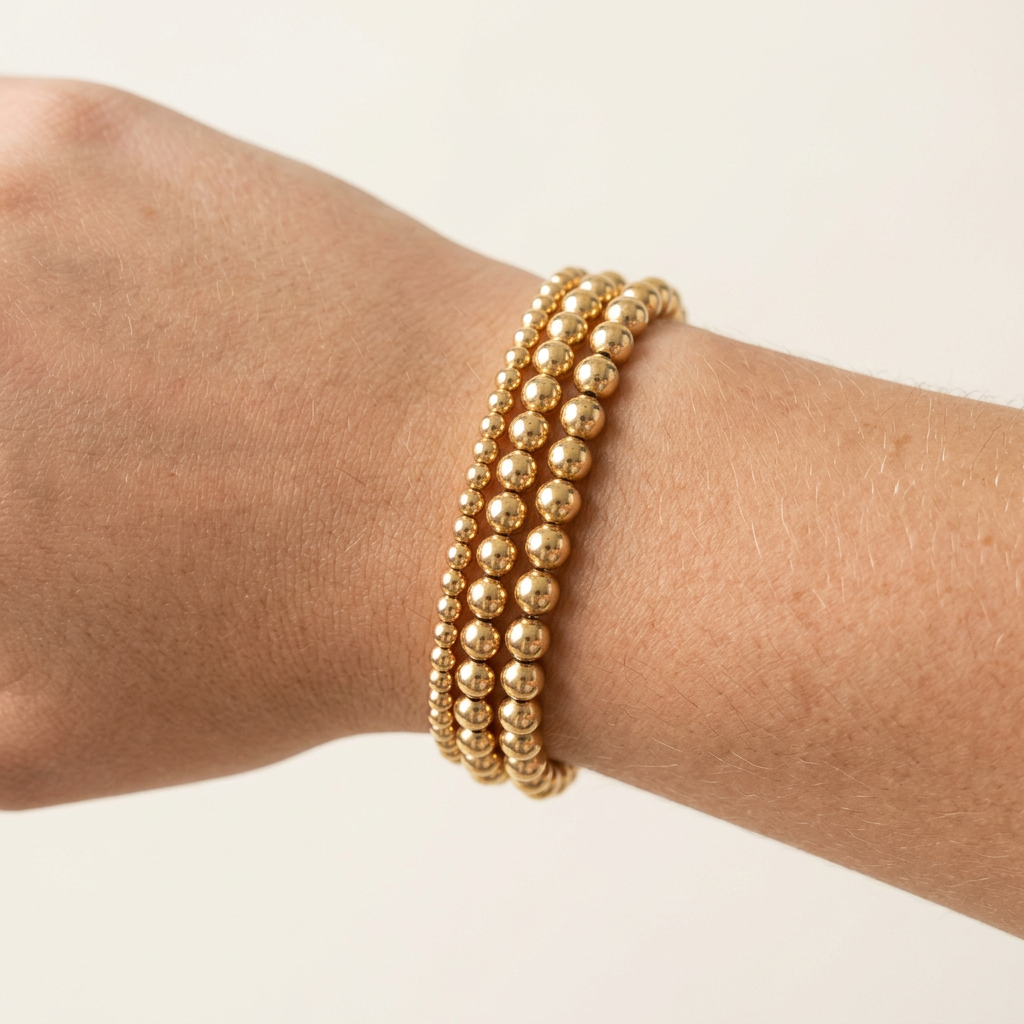 Three 14-karat gold-plated beaded bracelets with 6 mm, 4 mm, and 3 mm beads stacked on a wrist.