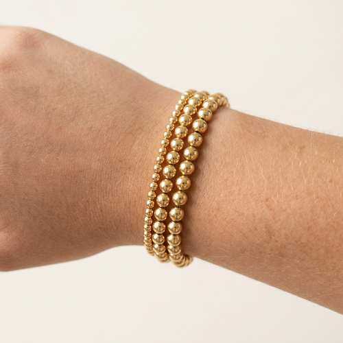 Three 14-karat gold-plated beaded bracelets with 6 mm, 4 mm, and 3 mm beads stacked on a wrist.