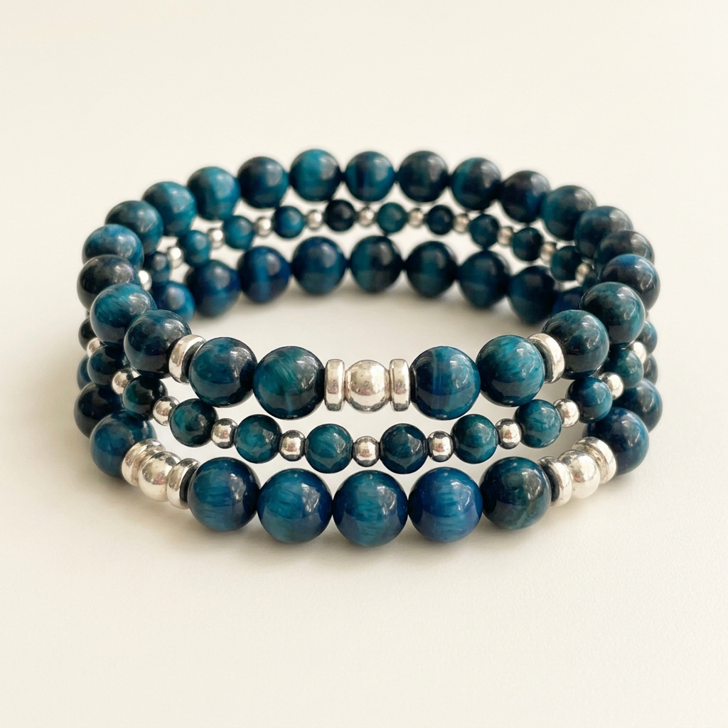 Three aquamarine tiger eye bracelets with silver spacers arranged in a stack on a soft ivory background