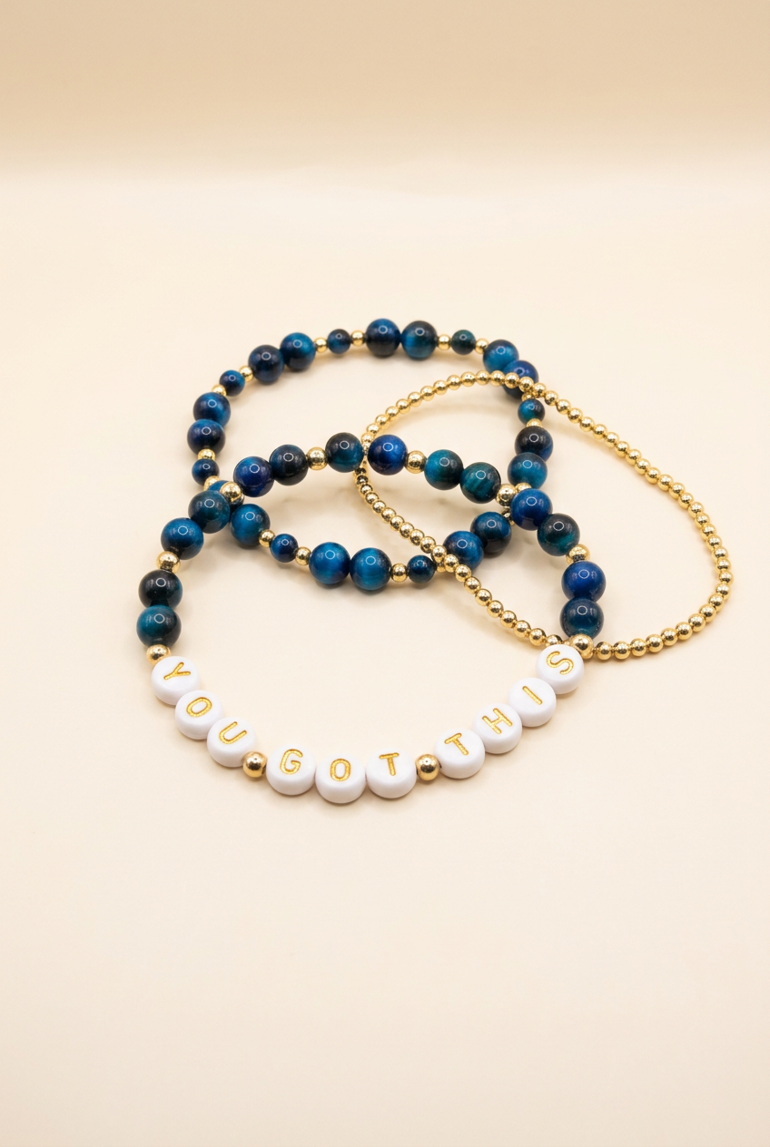 Blue tiger eye three-bracelet set with YOU GOT THIS letter beads and a gold-plated bracelet on ivory