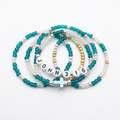 Teal and translucent white beaded faith bracelets with letter-bead accents and a cross detail on a white background.