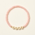 Blush-pink Hope handmade seed bead bracelet with cream letter beads on an ivory background