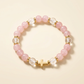 Pink and clear quartz bracelet with gold-plated spacers and a gold-plated cross on a soft cream background