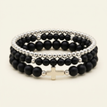 Three black onyx and silver-toned bracelets stacked on a warm ivory background