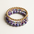 Purple blue imperial jasper and gold-plated bracelets arranged in a stack on a soft ivory background