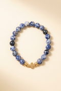 Blue jasper bead bracelet with a gold-colored cross on a warm ivory background
