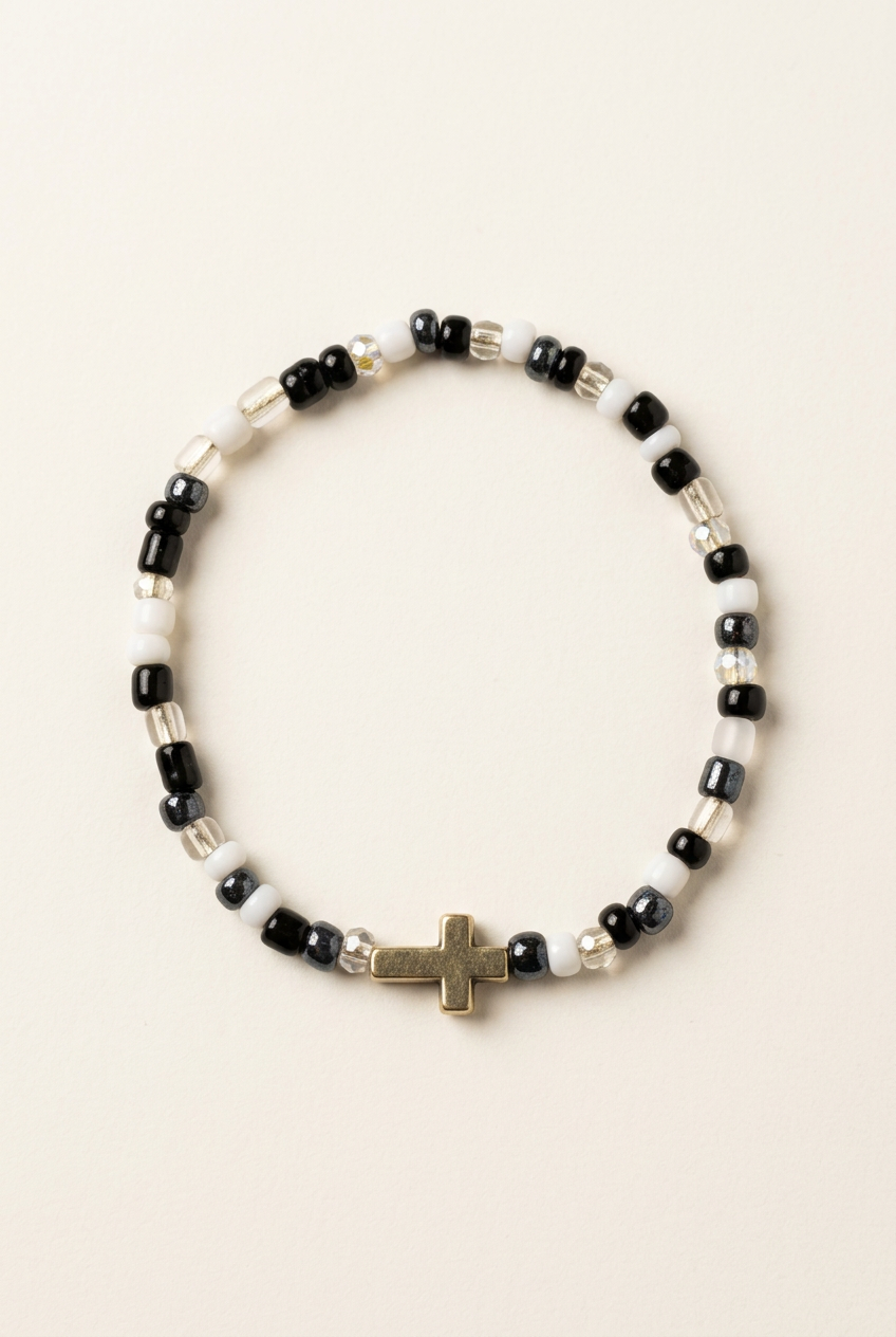 White, black, and clear seed bead bracelet with a silver cross on an off-white background