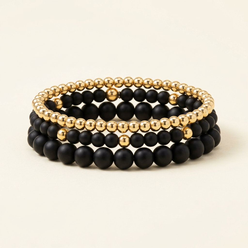 Handmade stack of three black onyx and gold-plated bracelets on a warm ivory background