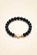 Single black Onyx bracelet with gold colored spacers and a gold colored cross on an ivory background