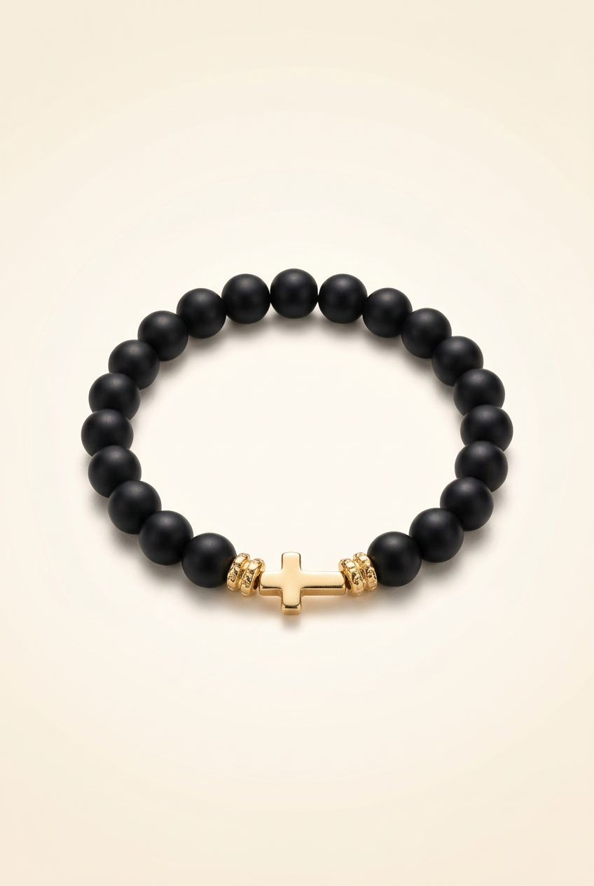 Single black Onyx bracelet with gold colored spacers and a gold colored cross on an ivory background