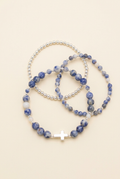 Three handmade blue jasper and silver-accented bracelets with a cross on a warm ivory background