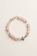Pink quartz and clear quartz bracelet with a silver-colored cross on an off-white background