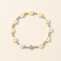 Handmade daisy bracelet with silver-plated beads and a silver-colored cross at the bottom center on an ivory background