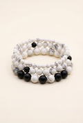 Handmade howlite and black onyx three-bracelet stack on warm ivory, with white beads separating the black bead groups on the bottom bracelet