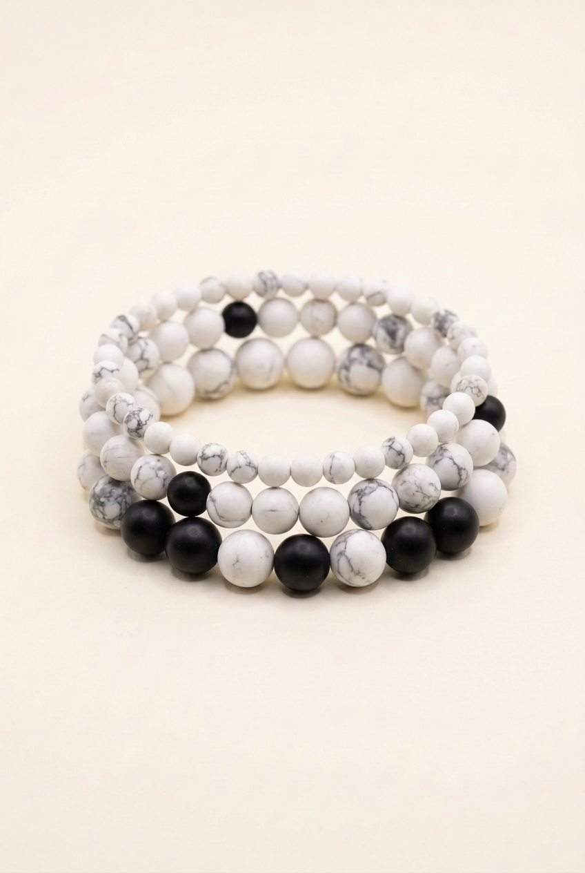 Handmade howlite and black onyx three-bracelet stack on warm ivory, with white beads separating the black bead groups on the bottom bracelet