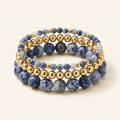 Three handmade blue spot jasper and gold-plated bracelets stacked on a warm ivory background