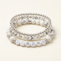 Handmade howlite and silver three-bracelet stack with STRONG letter beads on a warm ivory background