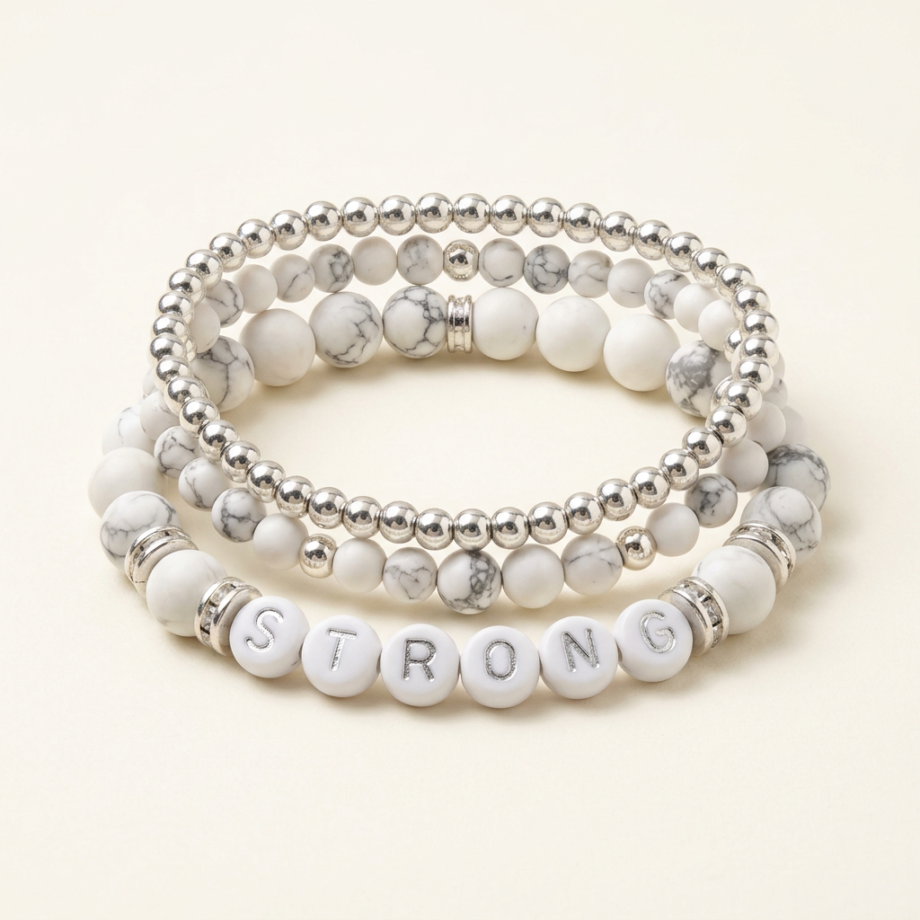 Handmade howlite and silver three-bracelet stack with STRONG letter beads on a warm ivory background