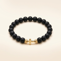Black onyx bracelet with a gold-tone cross on a warm-white background